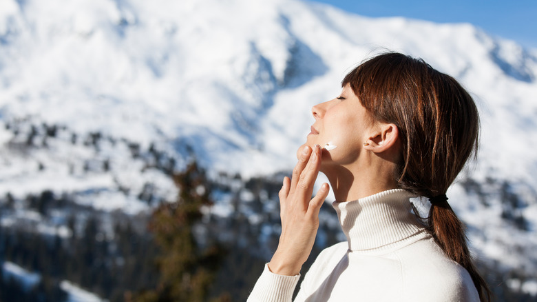 A woman in mountains putting moisturizer on her face