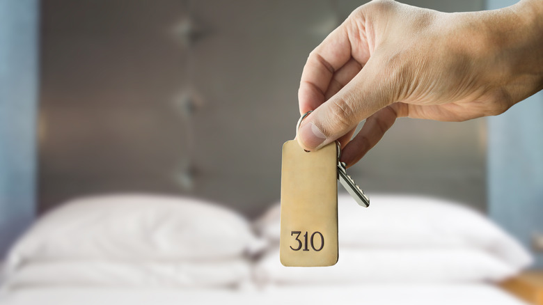 guest holding a hotel key in front of a bed in a hotel room