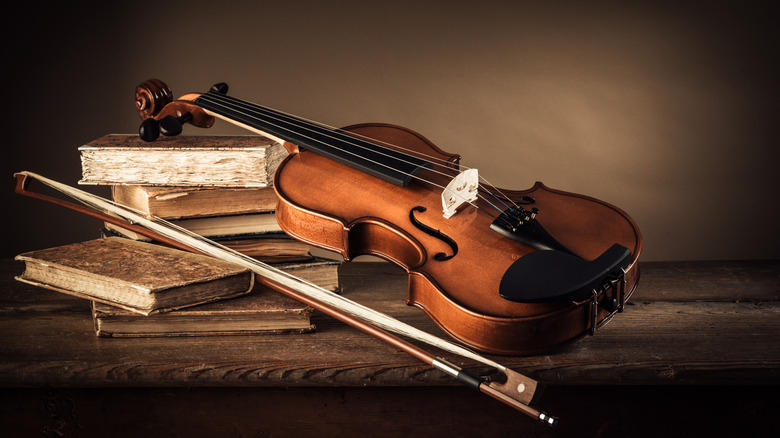 Books stacked next to an antique violin with a bow