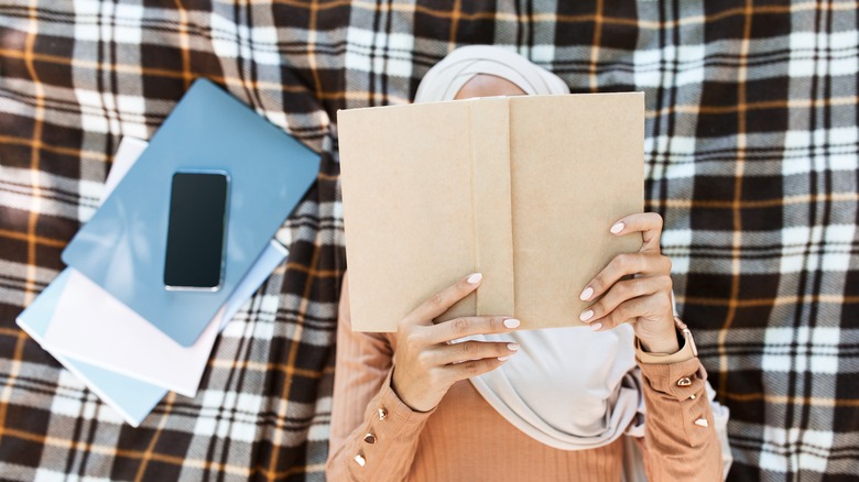 Woman in hijab reading book on blanket 