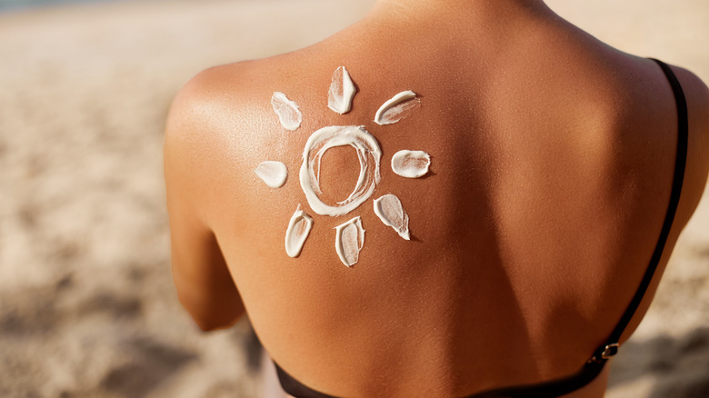 Sunscreen applied in shape of sun on back of tan woman