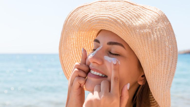 Smiling woman wearing a straw hat and applying sunscreen.