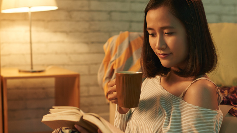 woman sitting on a couch with a mug of tea reading a book