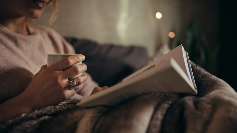 Cropped picture of a woman's hands as she holds a mug and a book