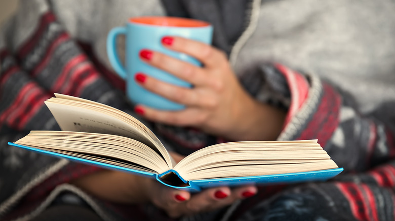 woman with painted red nails holding a mug and an open book