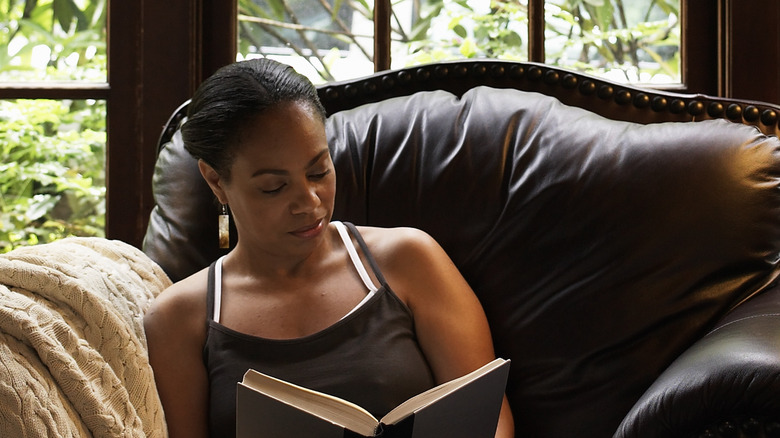 Black woman sitting in a luxe leather chair reading a book in front of a wall of windows