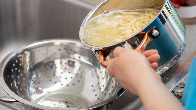 Woman pouring pasta into a colander in the sink