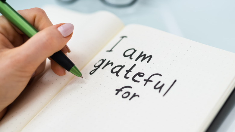 Woman writing "I am grateful for" in a journal