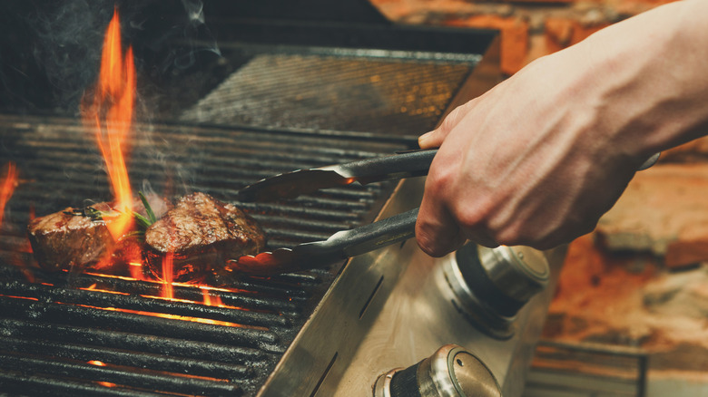 A chef using tongs to flip a steak