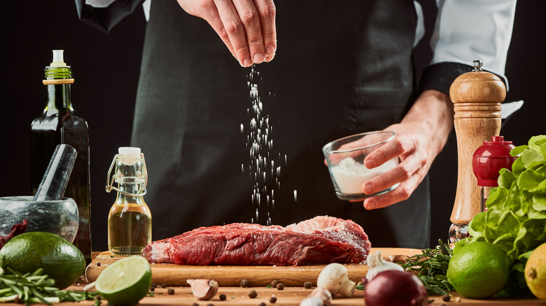 A chef seasoning a steak