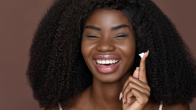 Woman smiling with moisturizer on fingertip