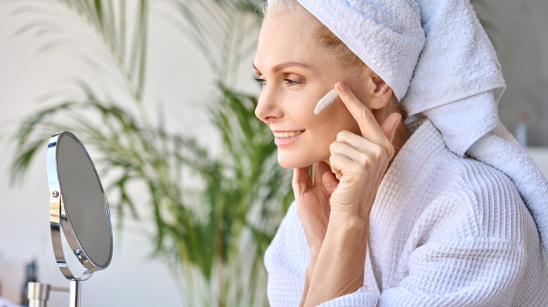 woman wearing towel applies moisturizer