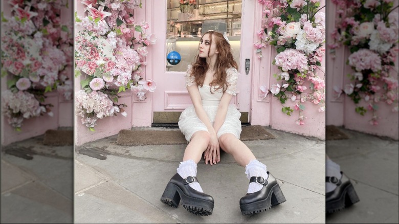 @larissa.fae.love sitting in front of pink doorway in frilly dress