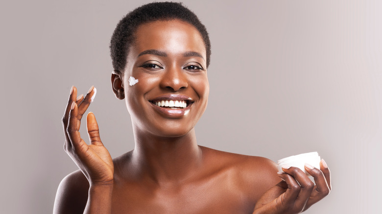 Young woman smiling as she applies face cream