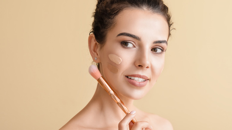 Woman with foundation on her face and a makeup brush in her hand