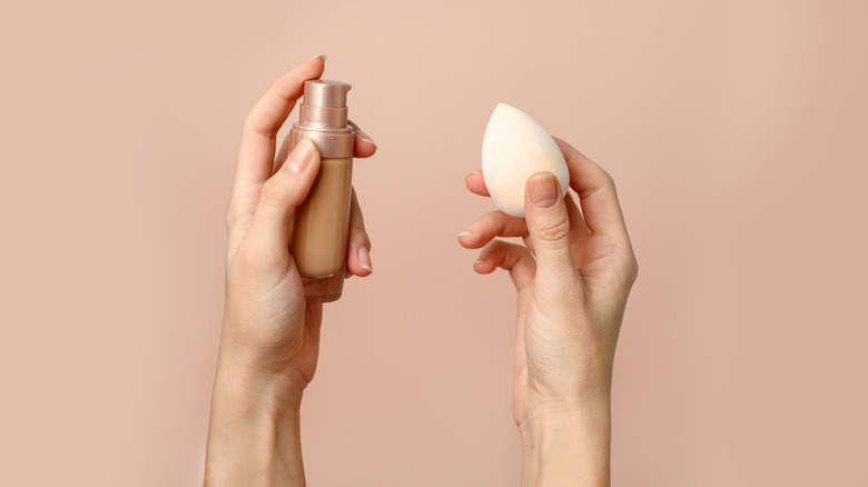 Woman holding a makeup sponge and a foundation in each hand