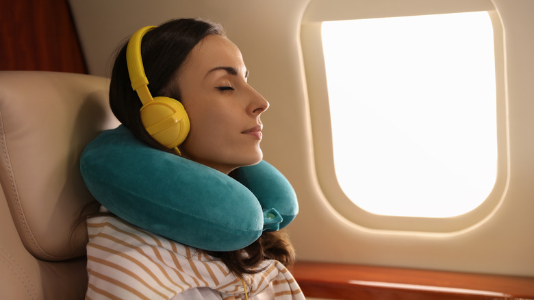 A woman using a neck pillow and headphones. 