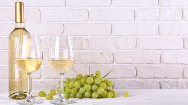 Bottle of white wine with two filled glasses beside green grapes on a white counter 