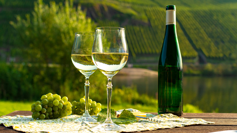 A bottle of Riesling and two full glasses with a vineyard backdrop 