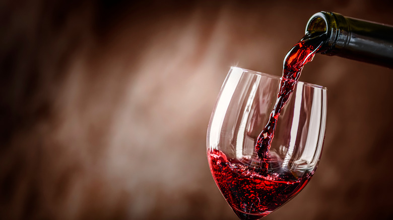 A bottle of red wine being poured into a glass 