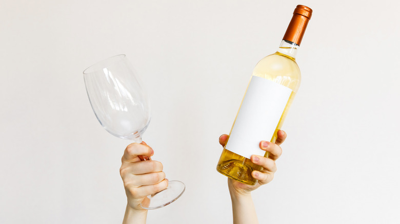 Woman holding a wine glass in one hand and a bottle of white wine in the other