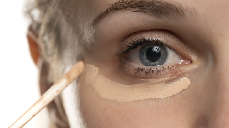 Woman applying concealer under eyes