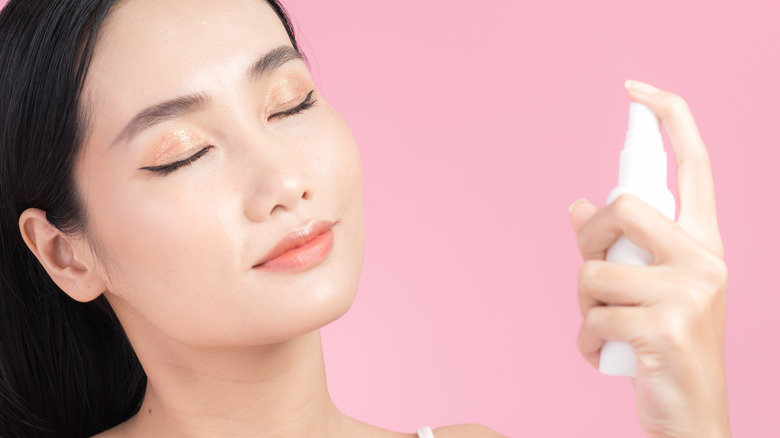 Woman applying setting spray to face