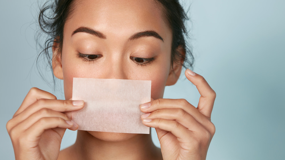 A woman oil blotting her skin