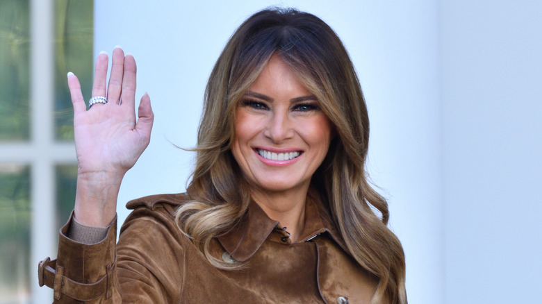 Melania Trump waving and wearing a brown leather coat