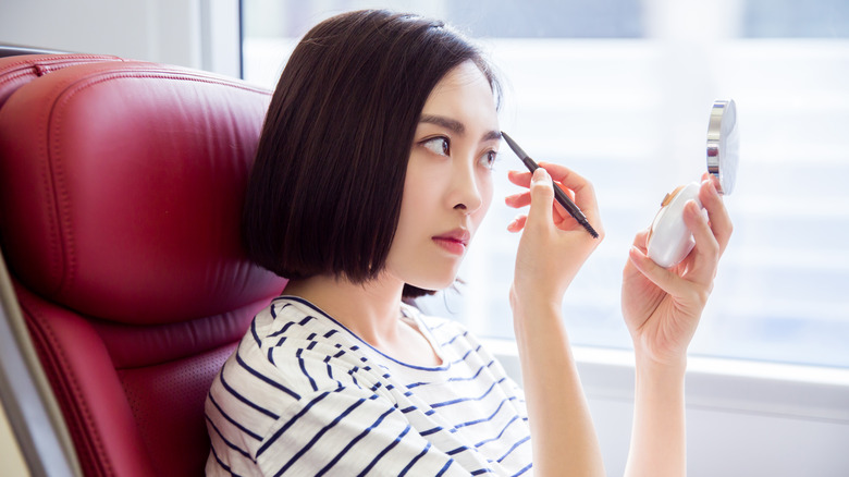 Woman doing her makeup in front of a window