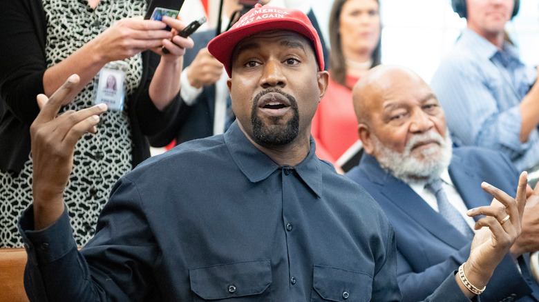 Kanye West in a MAGA hat with his hands up