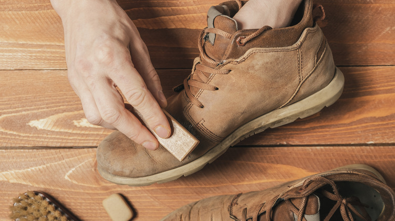 White hands brushing brown suede boots