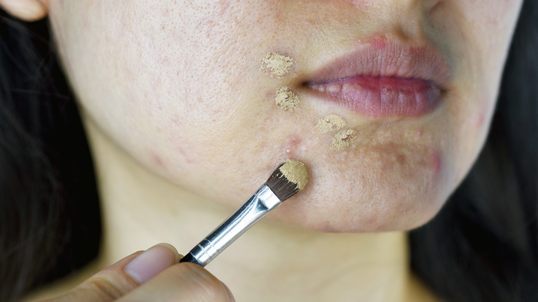 woman uses brush to apply concealer on blemishes