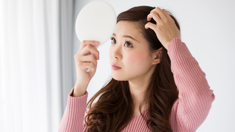 Woman looking at hair part in mirror