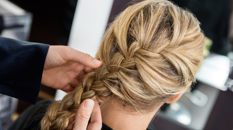 Hairdresser holding a blonde woman's French braid. 