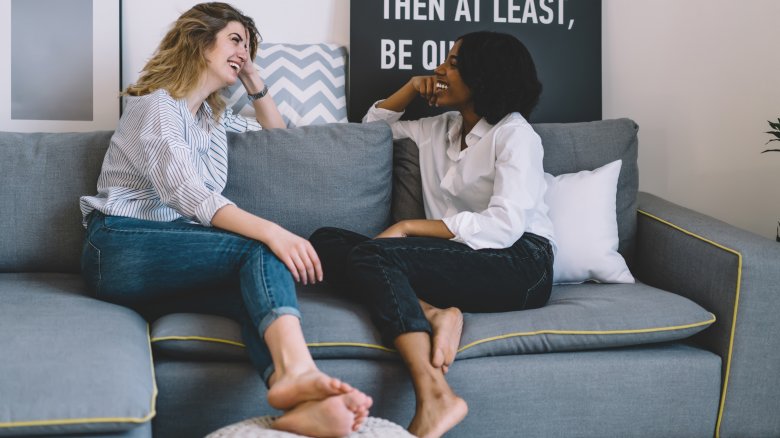 Two charming young women chatting barefoot on a couch