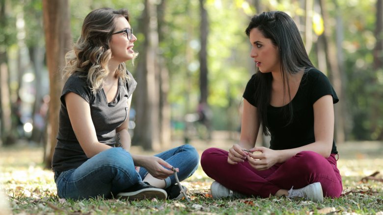 Young women sitting on ground with legs crossed speaking