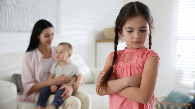 A girl looking upset as her mother holds her sibling