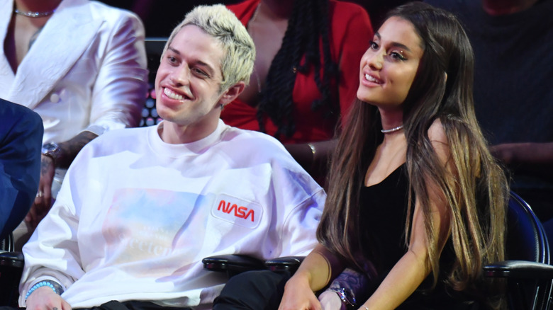 Pete Davidson and Ariana Grande smile while sitting next to each other