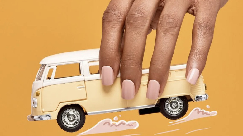 Woman with press on nails holds a yellow bus toy 