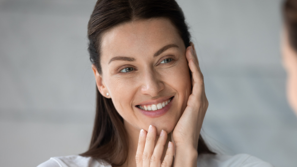 Woman looking into the mirror and smiling while touching her face 