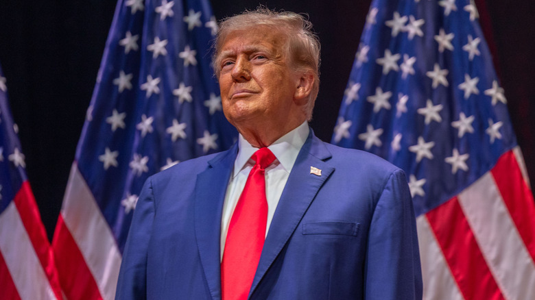 Donald Trump stands in front of three American flags