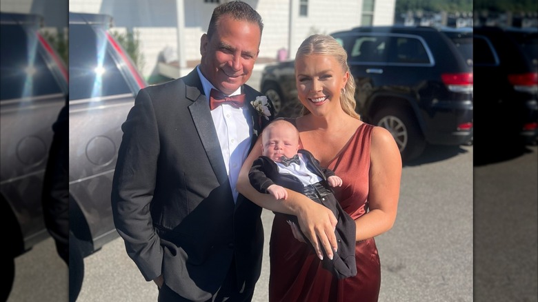 Karoline Leavitt in brown dress holding baby and smiling with husband Nicholas Riccio in tux