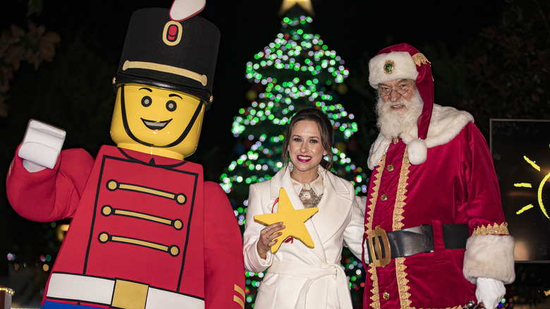 Lacey Chabert standing in front of a christmas tree in between santa and lego soldier