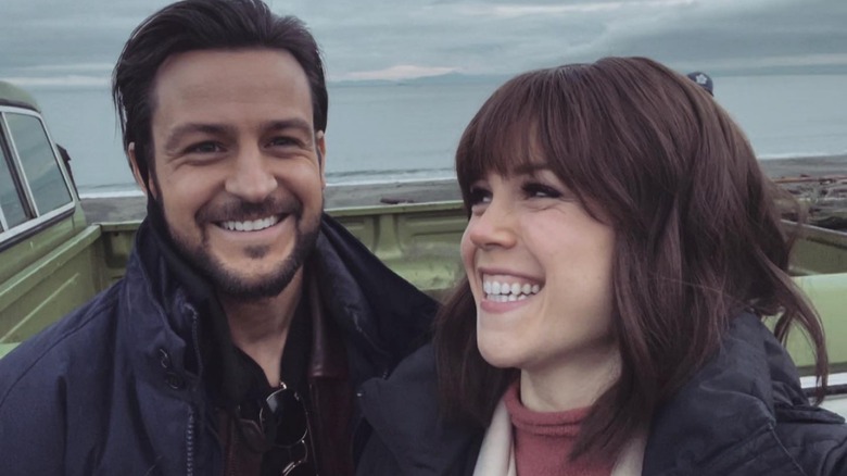 Tyler Hynes and Erin Krakow smiling together in a cloudy beach setting