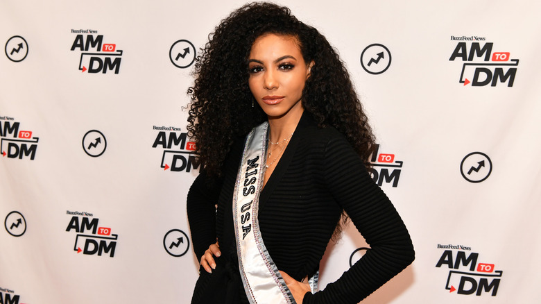 Cheslie Kryst poses with her Miss USA sash while wearing a long-sleeve black dress.