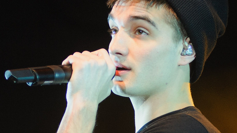 tom parker of the wanted  holding a microphone onstage