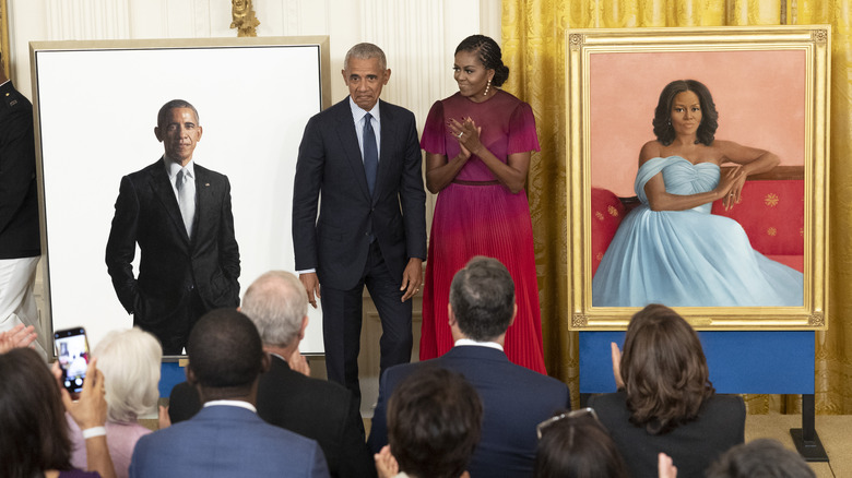 Barack and Michelle Obama standing next to their portraits