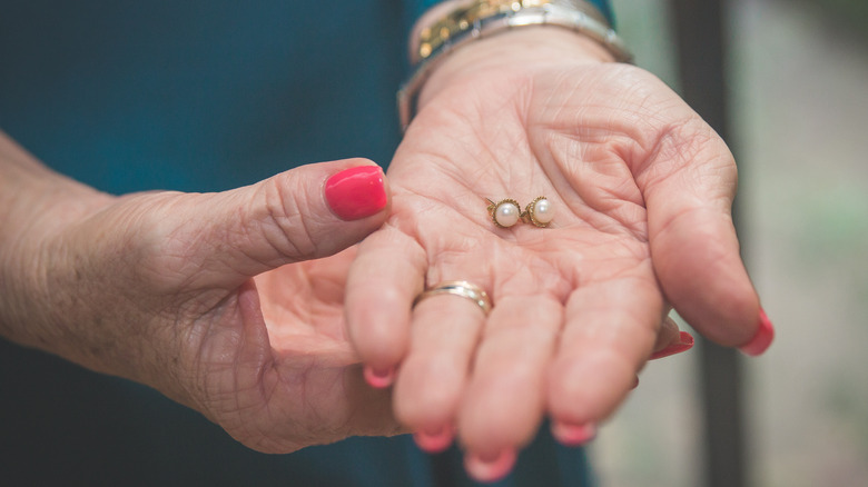 Older woman holds a pair of pearl earrings in her hand