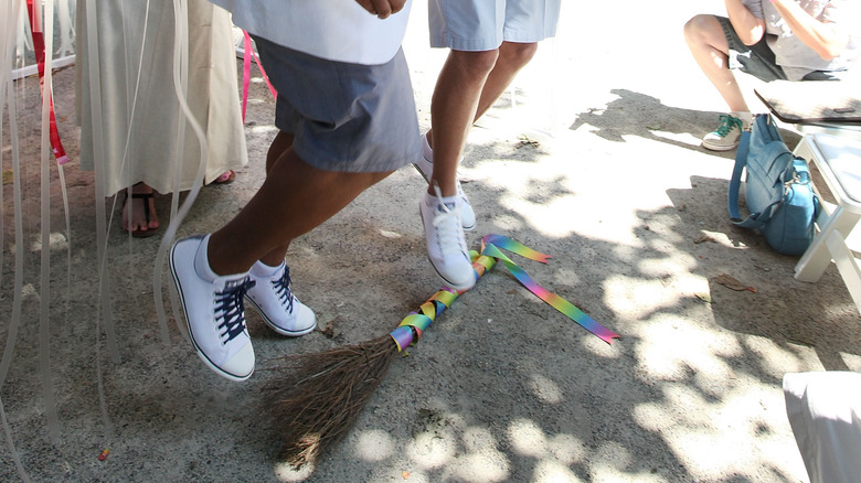 Same-sex couple celebrates their marriage by jumping the broom wrapped in rainbow ribbon